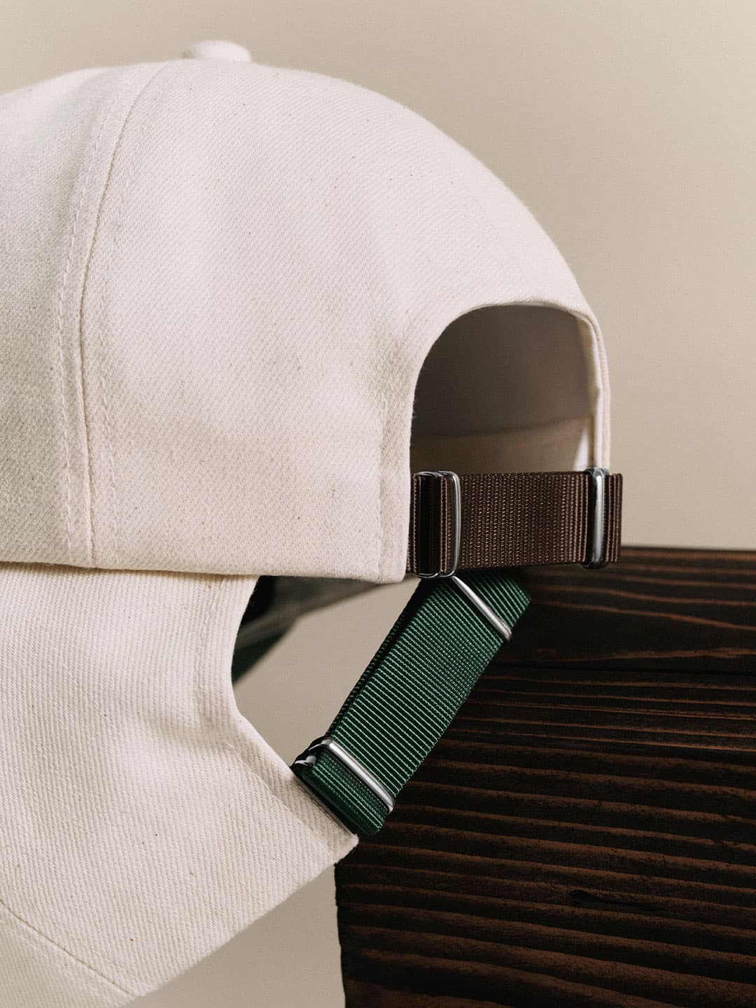 Close-up of a white baseball cap with adjustable brown and green straps resting on a dark wooden surface.