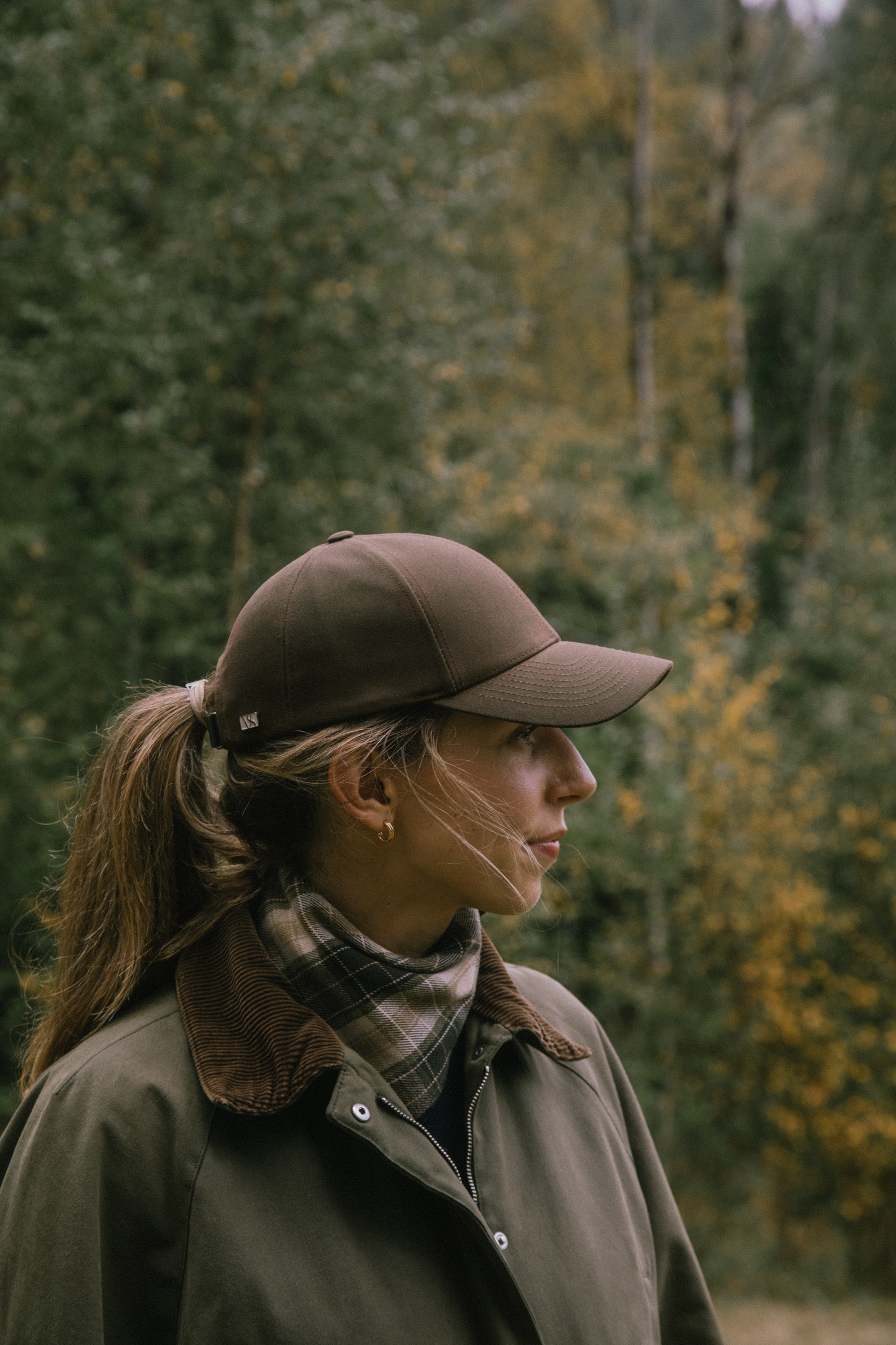 Side view of female wearing a brown oilskin cap from Varsity Headwear in the woods in Norway